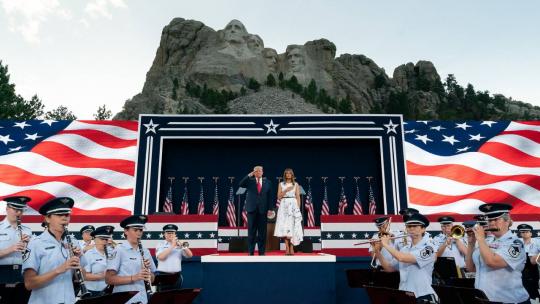 President Trump salutes and First Lady Melania Trump places her hand on her heart as the US Air Force Academy Concert Band performs the National Anthem during a Fourth of July celebration Friday, July 3, 2020, at Mount Rushmore National Memorial.